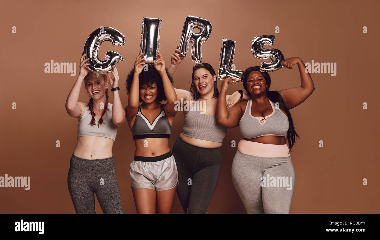 Multi-ethnic group of women holding girl word in balloon letters against brown background.  Focus on girl word in balloon letters. Stock Photo