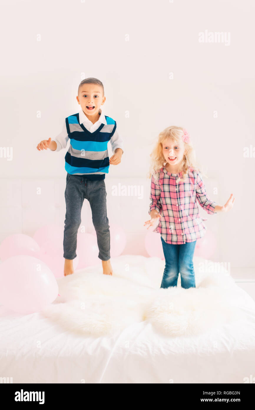 Group portrait of two happy white Caucasian cute adorable funny children jumping on bed in bedroom. Boy and girl having fun together. Best friends for Stock Photo
