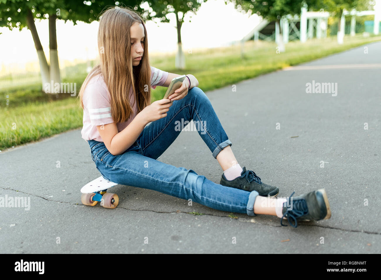 Teenager girl 8-13 years old, sitting on a skateboard in a city park in the...