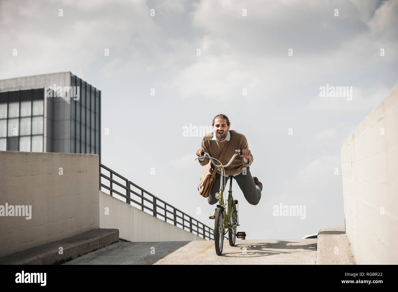Laughing businessman riding down a ramp on his bicycle Stock Photo