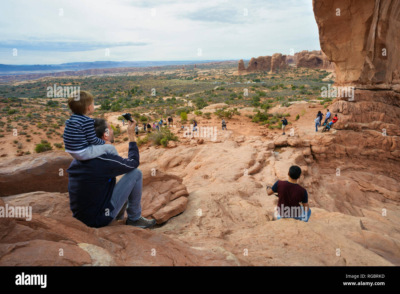 Man taking a picture of North Window Arch with a child perched  on his shoulders, Arches National Park, Utah, USA. Stock Photo