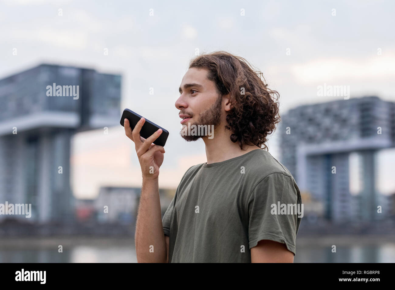 Germany, Cologne, young man using smartphone at the riverside Stock Photo