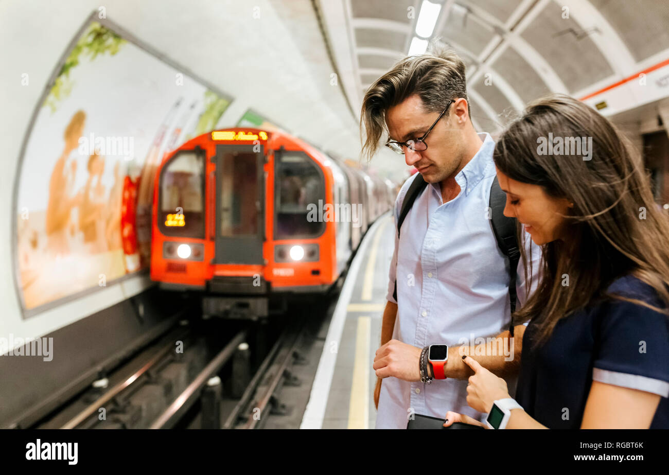 UK, London, couple waiting at   underground station platform looking at smartwatch Stock Photo