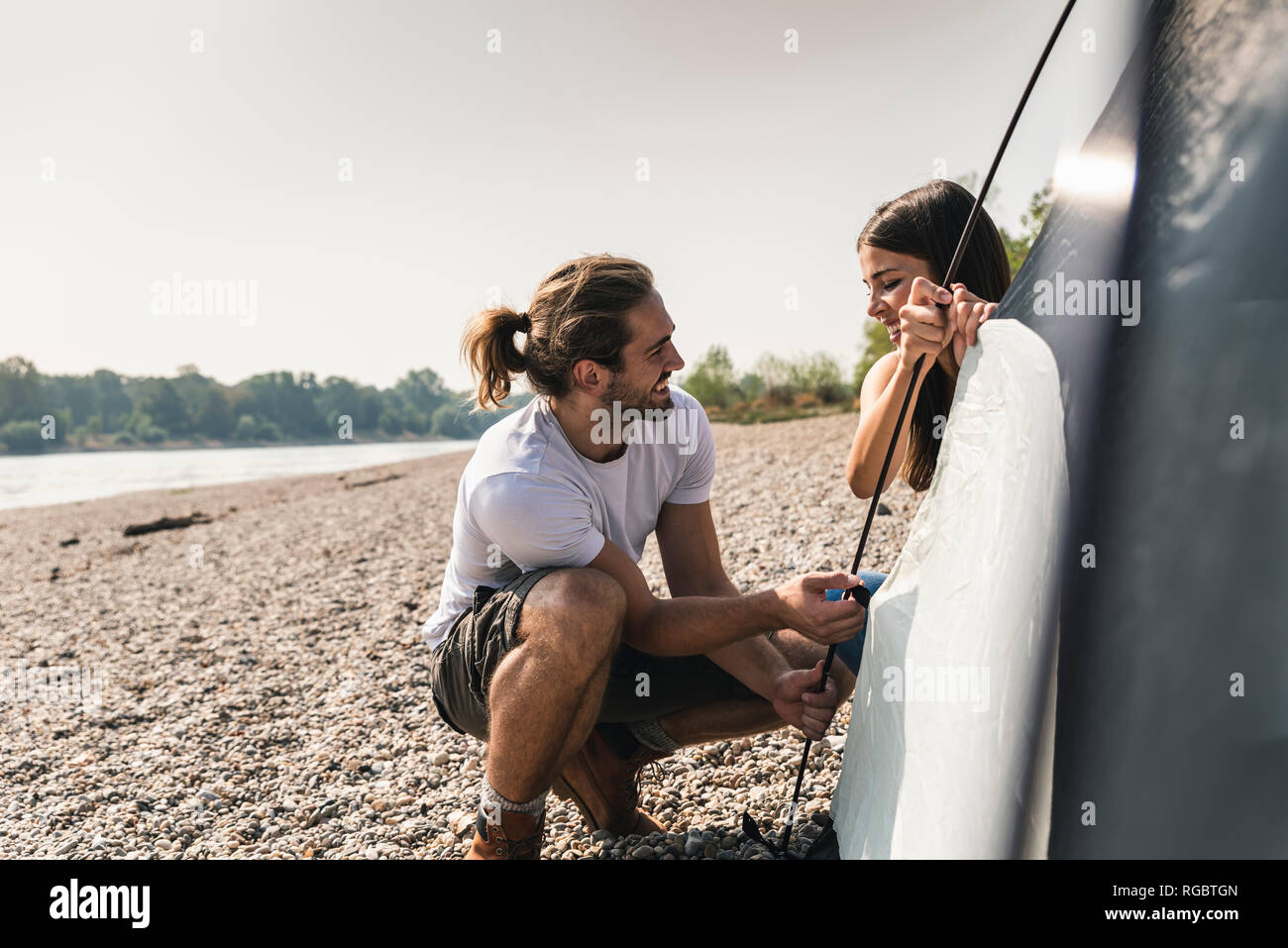 Smiling young couple setting up a tent at the riverside Stock Photo