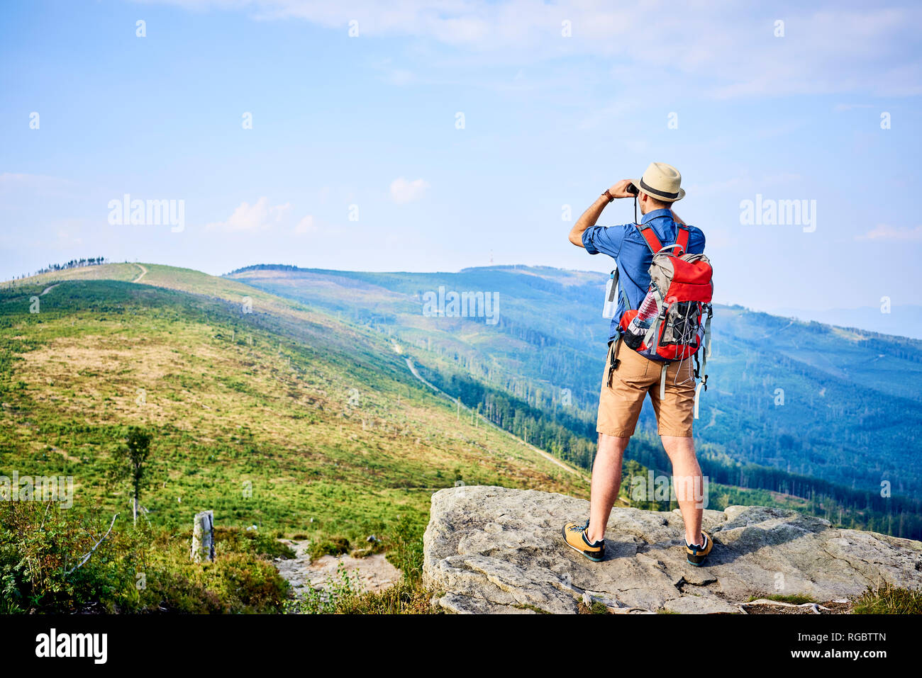 Rear view of man looking through binoculars during hiking trip Stock Photo
