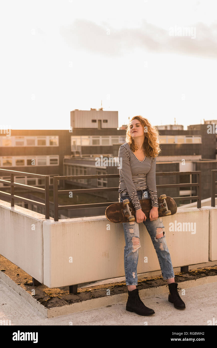 Young woman with skateboard enjoying sunset on roof terrace Stock Photo