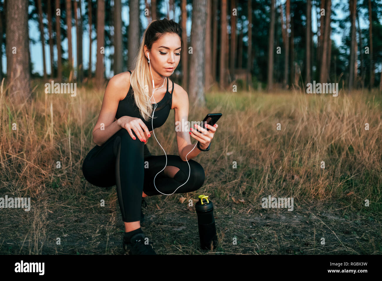 Beautiful girl athlete, sat down rest in forest on background of trees, in  fresh air. morning jogging in summer park. In hands of the phone and Stock  Photo - Alamy