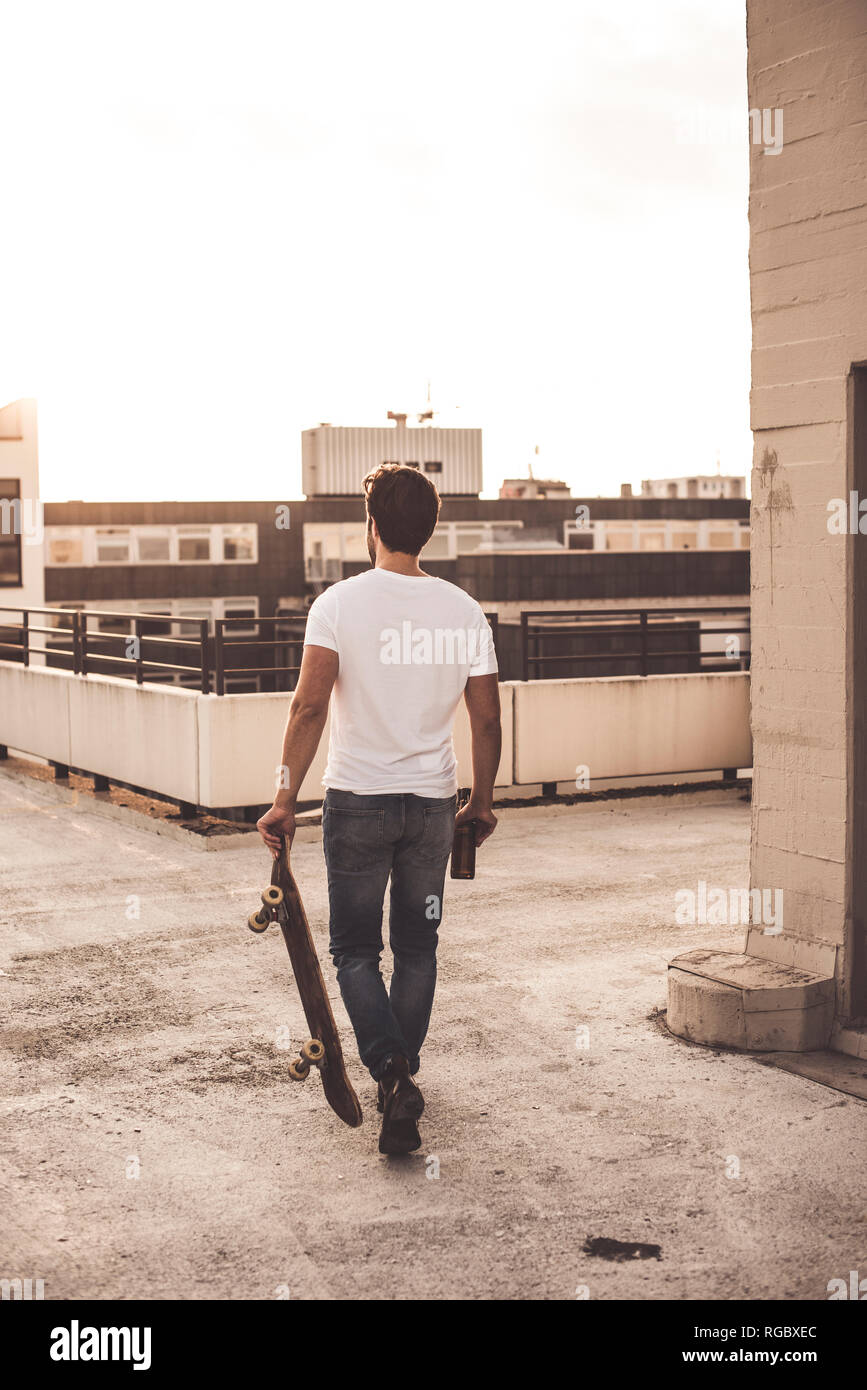Back view of young man with skateboard and beer bottle on roof terrace at  evening twilight Stock Photo - Alamy