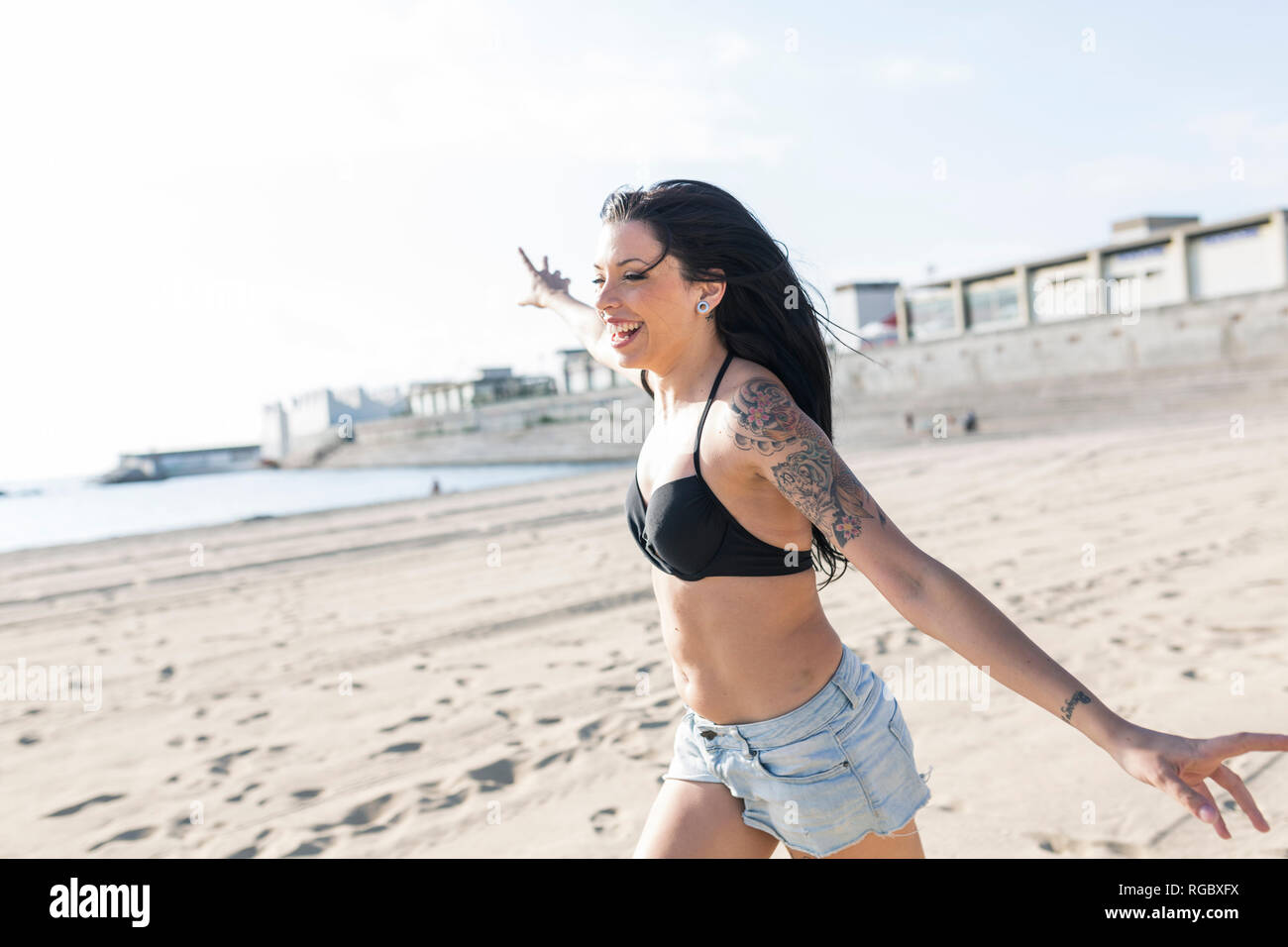 Happy young woman with tattoo running on the beach Stock Photo - Alamy