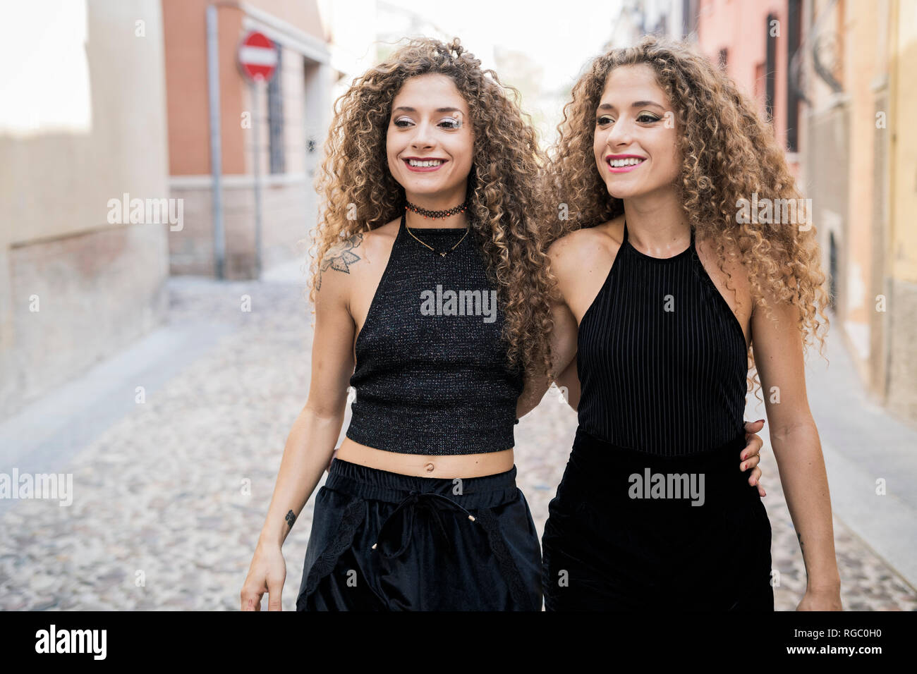 Portrait of relaxed twin sisters dressed in black walking arm in arm in the city Stock Photo