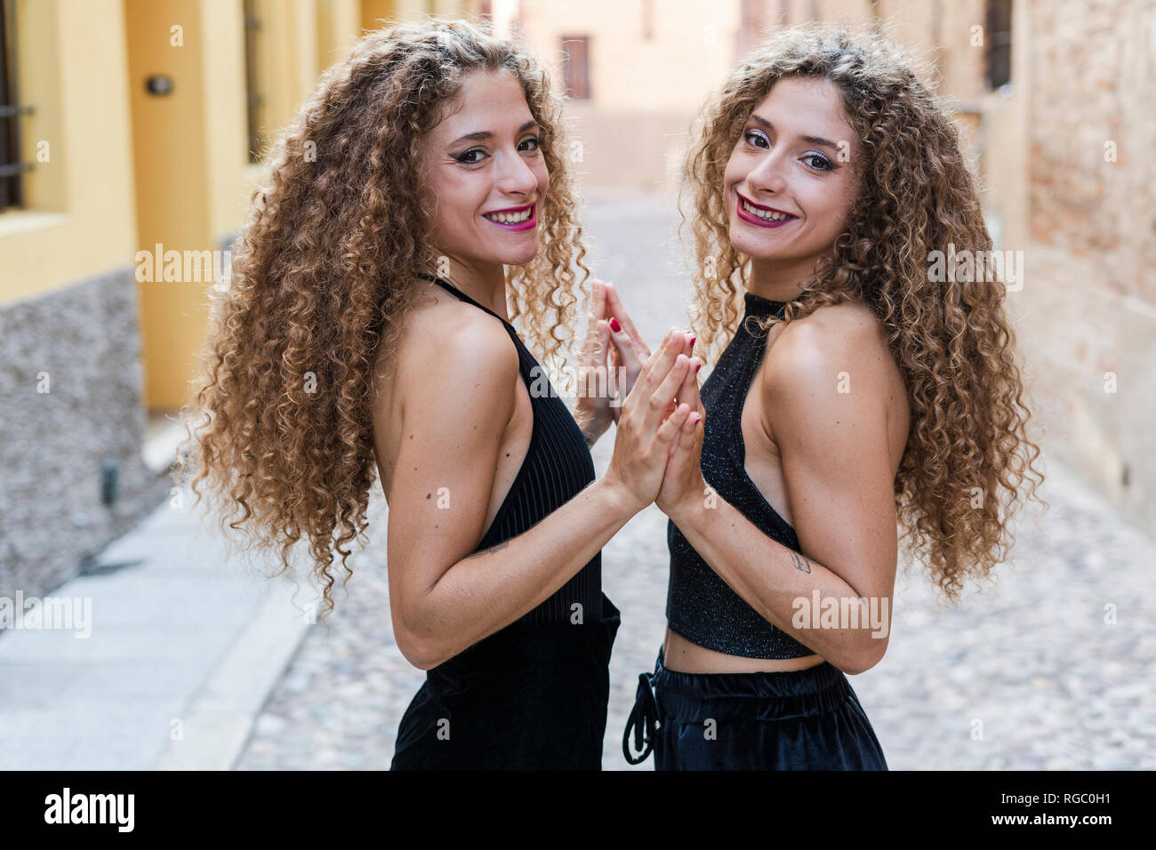 Portrait of happy twin sisters touching their hands Stock Photo