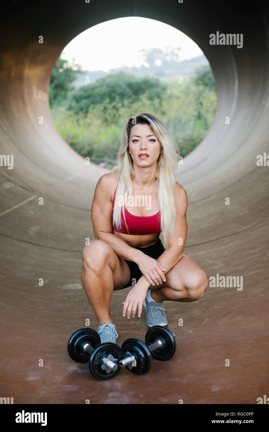 Athletic woman crouching inside a tube with dumbbells Stock Photo