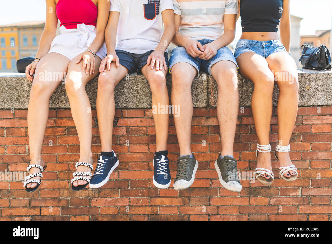 Legs of friends sitting together on a wall Stock Photo