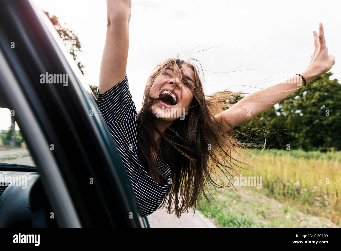 Carefree young woman leaning out of car window screaming Stock Photo