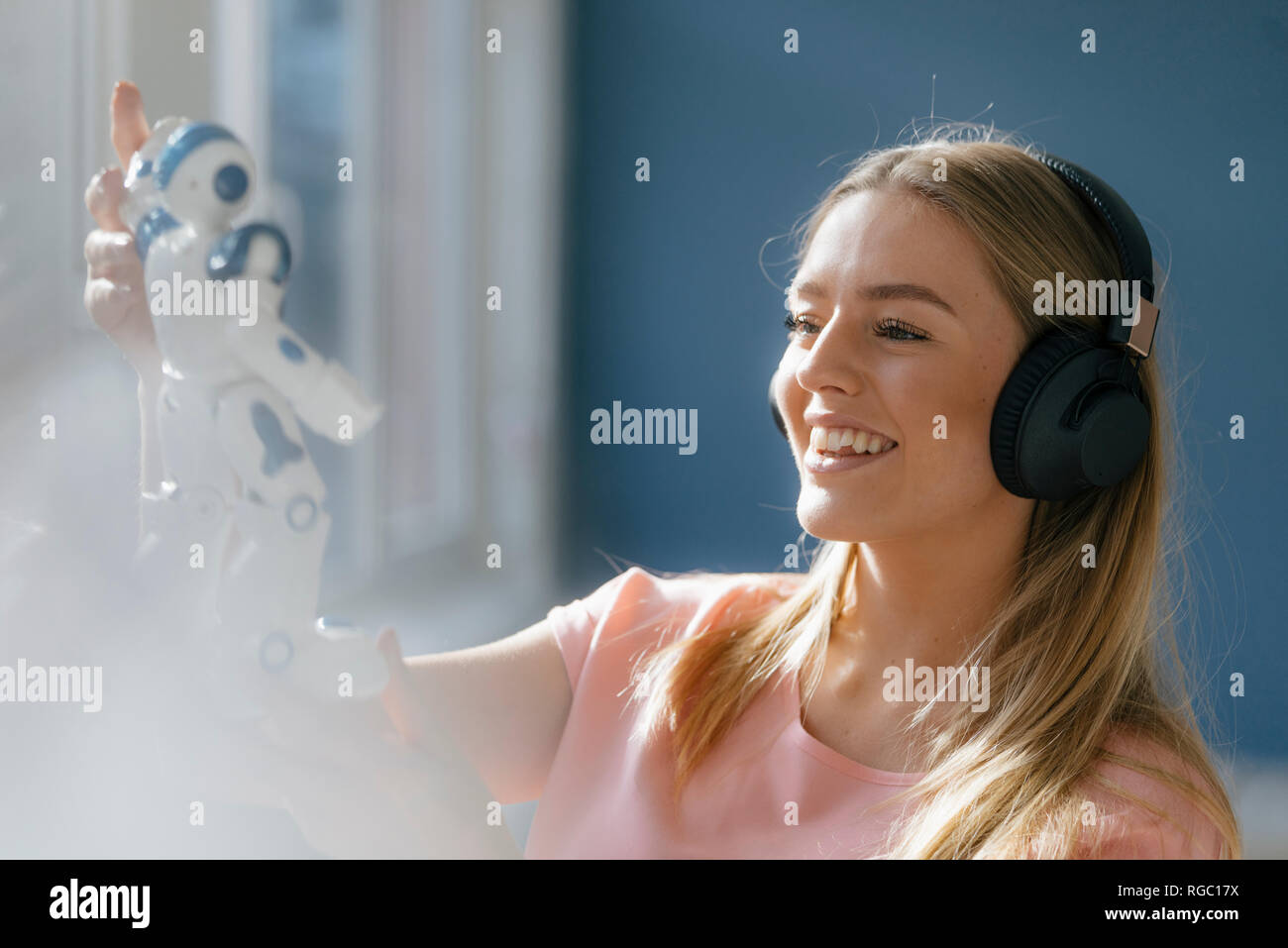 Portrait of smiling young woman with headphones looking at toy robot Stock Photo