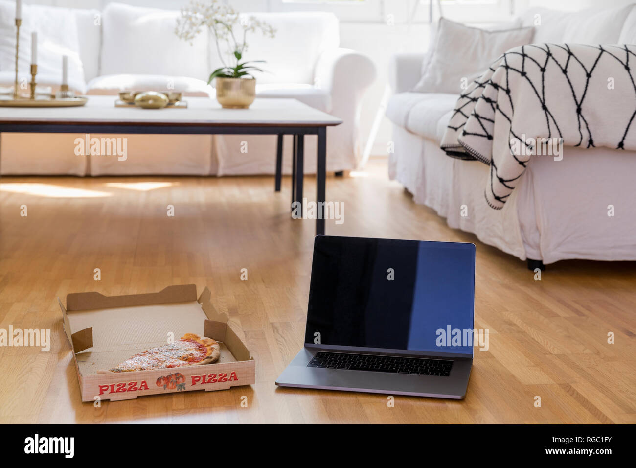 Pizza box with pizza and laptop standing on floor of living room Stock Photo