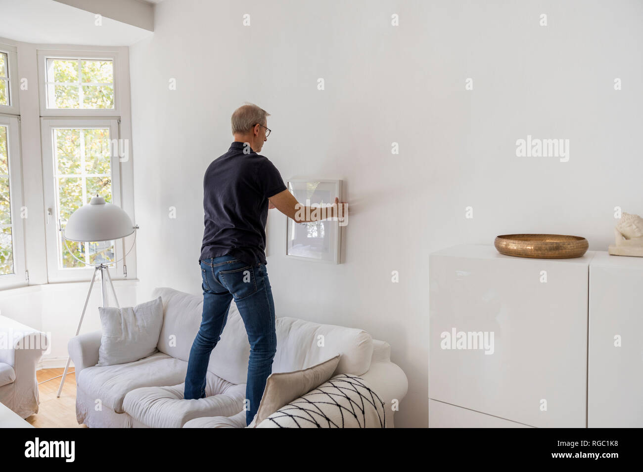 Back view of mature man hanging up picture frame at home Stock Photo