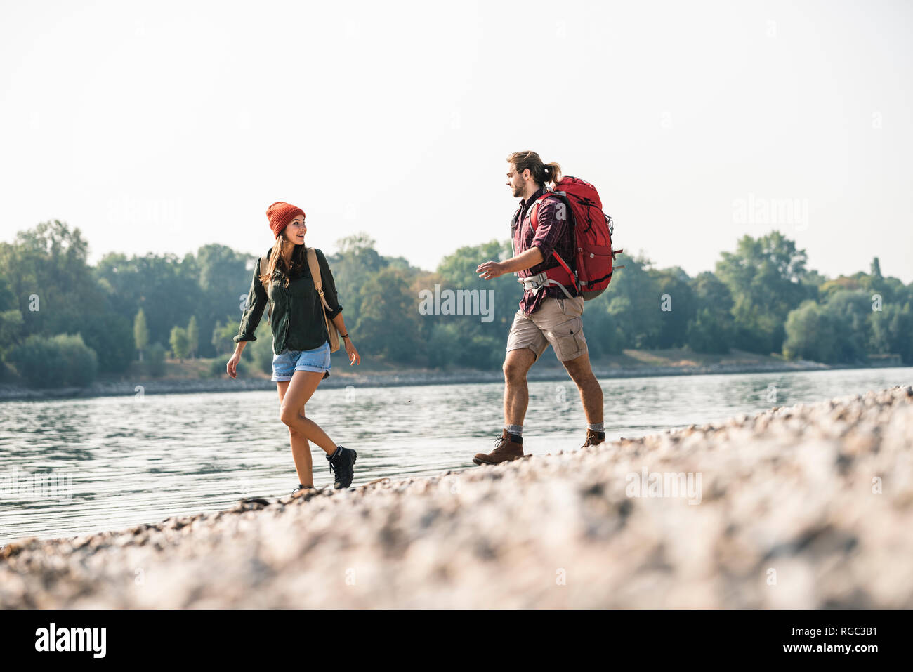 Young couple with backpacks walking at the riverside Stock Photo - Alamy