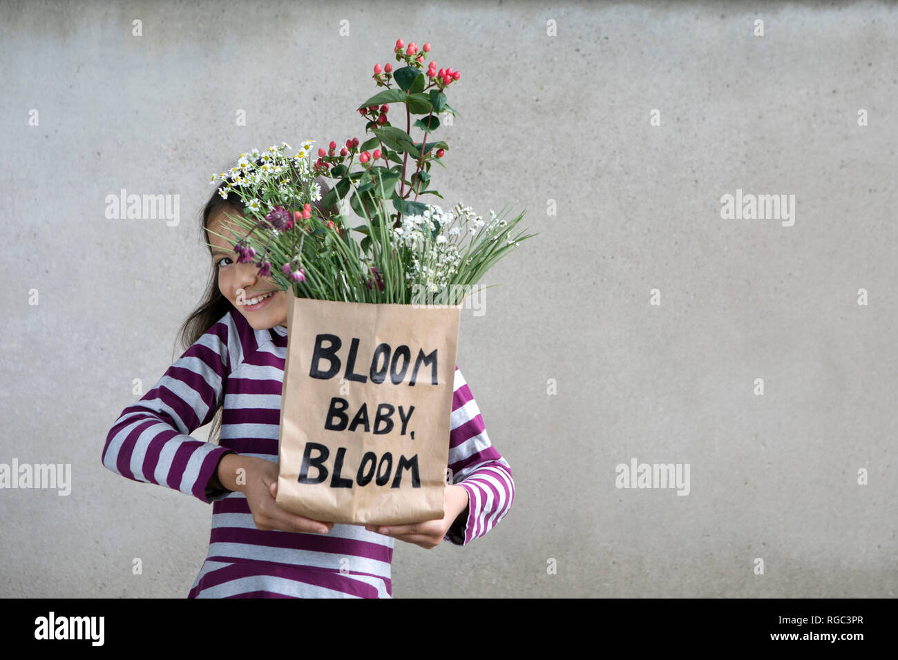 Smiling girl holding paper bag with flowers Stock Photo
