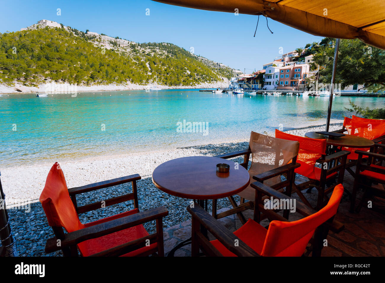 Tables with chairs of cozy Greek tavern restaurant in front of the beach in Assos village on Kefalonia island in Greece on summer morning Stock Photo