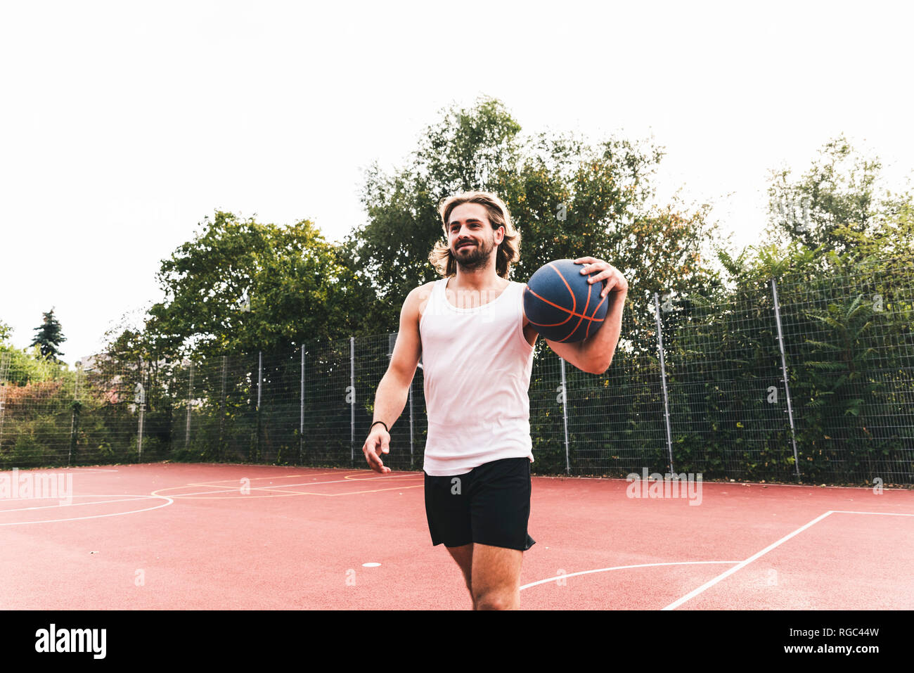 Young man leaving basketball ground, carrying ball Stock Photo