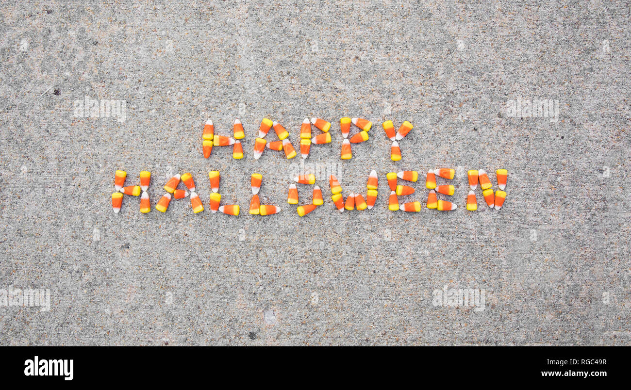 The phrase Happy Halloween spelled out with candy corn on a sidewalk. The phrase is centered in the photo. Stock Photo