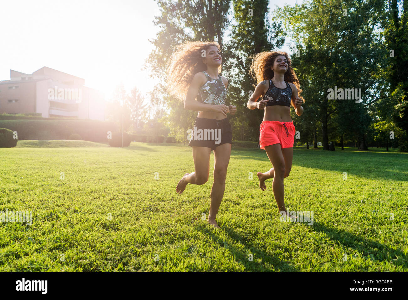 Twin sisters jogging barefoot on a meadow Stock Photo