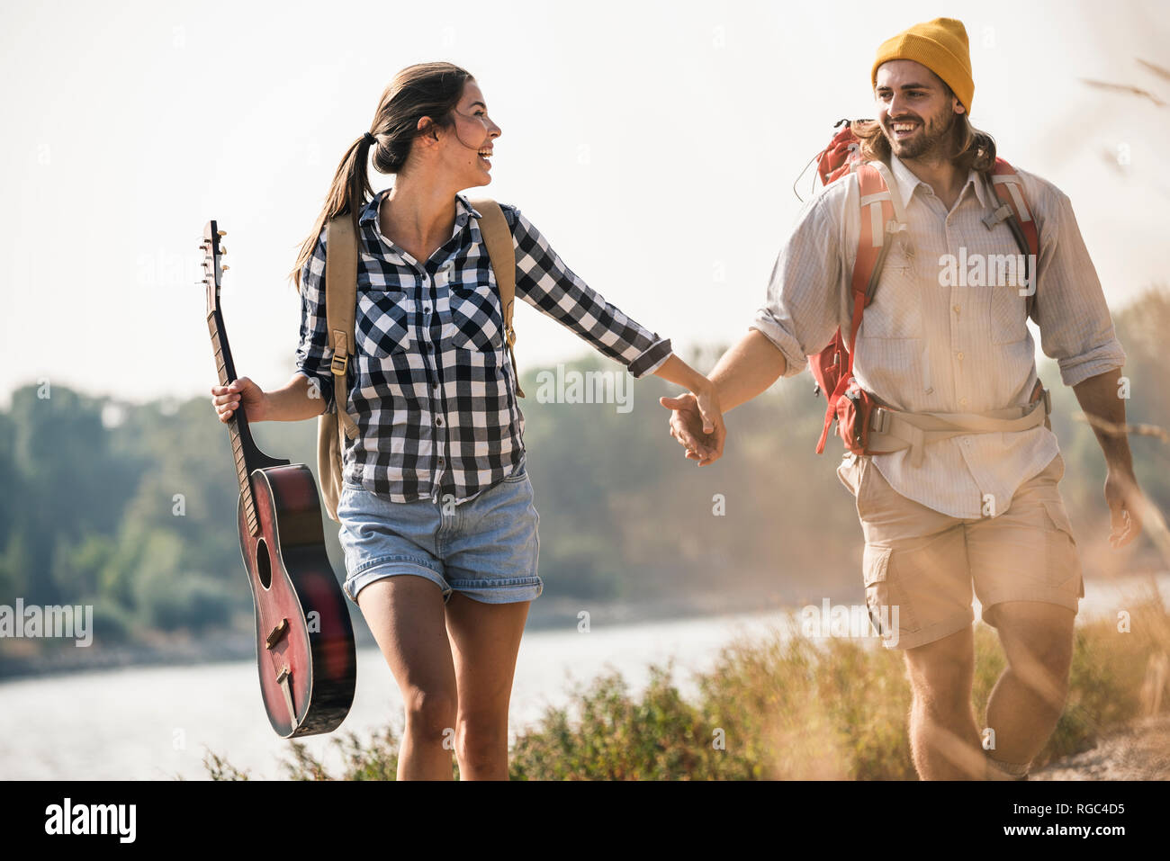 Happy young couple with backpacks and guitar walking at the riverside Stock Photo