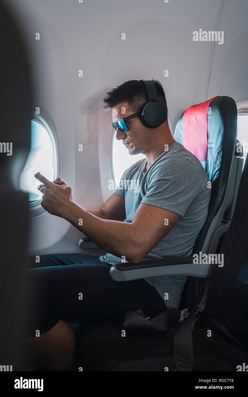 Man in airplane, using smartphone, headphones Stock Photo