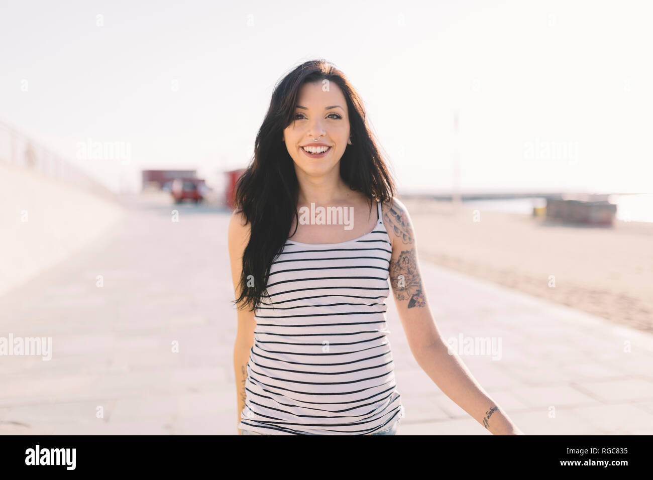 Portrait of smiling young woman with tattoo walking on beach promenade Stock Photo