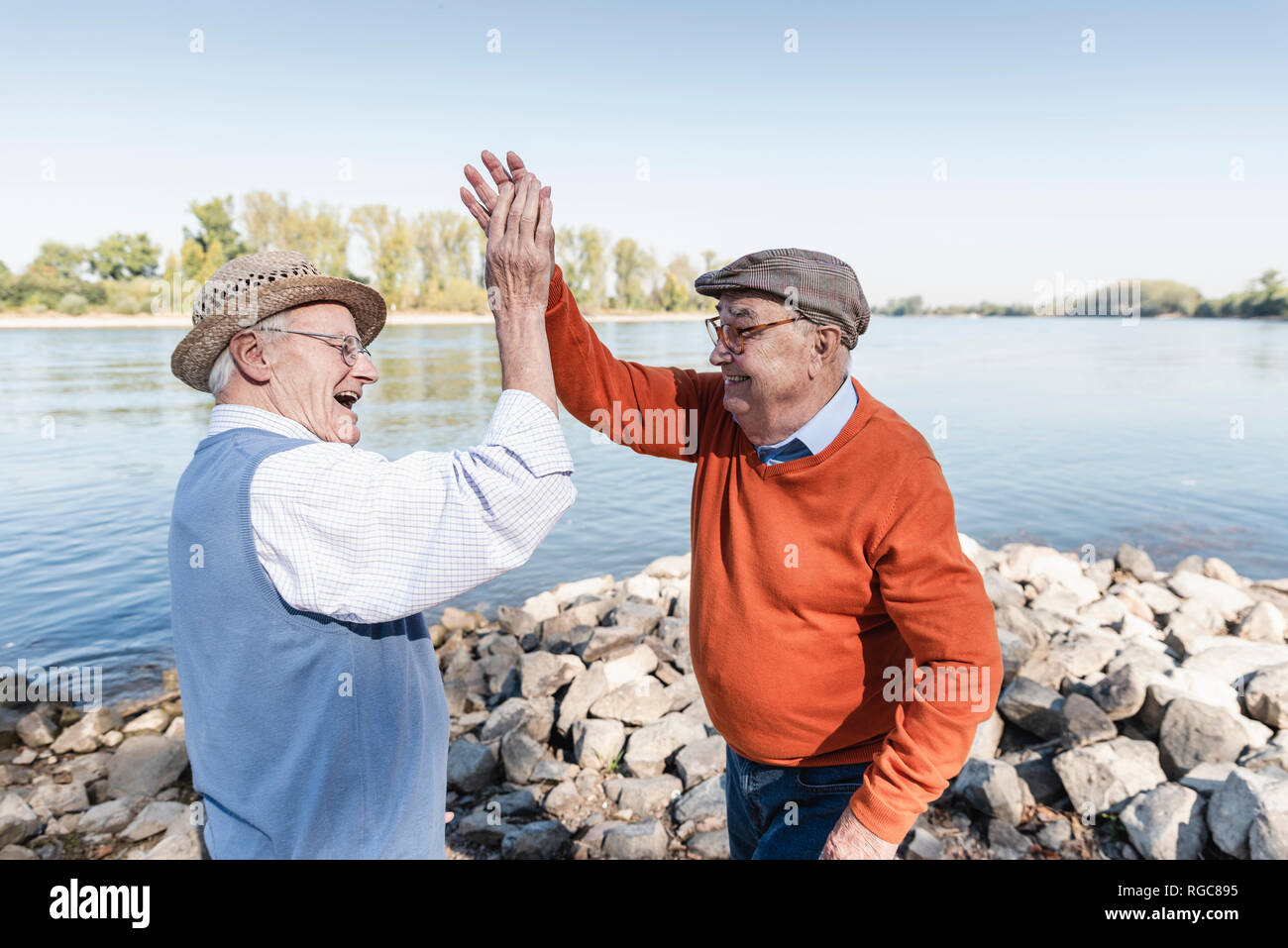 Two laughing old friends high-fiving at a lake Stock Photo