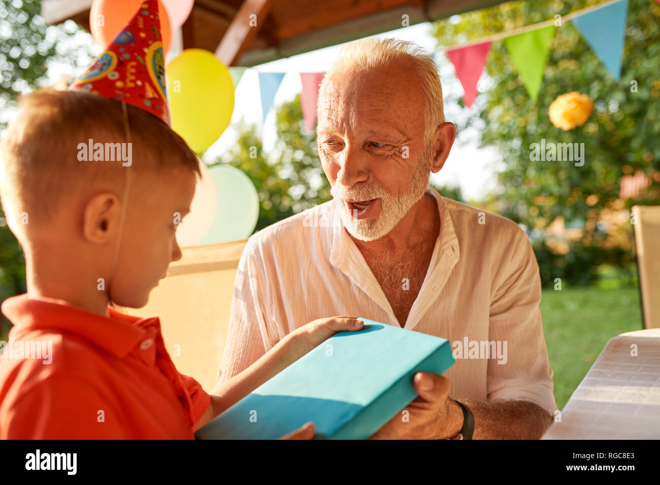 Grandfather handing over present to grandson on a garden birthday party Stock Photo