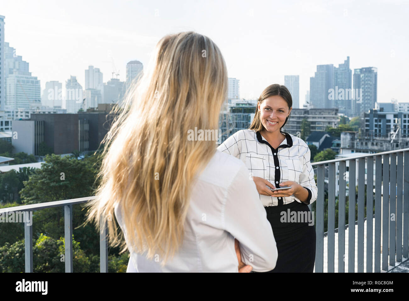 Two female colleagues speaking with each other on city rooftop Stock Photo