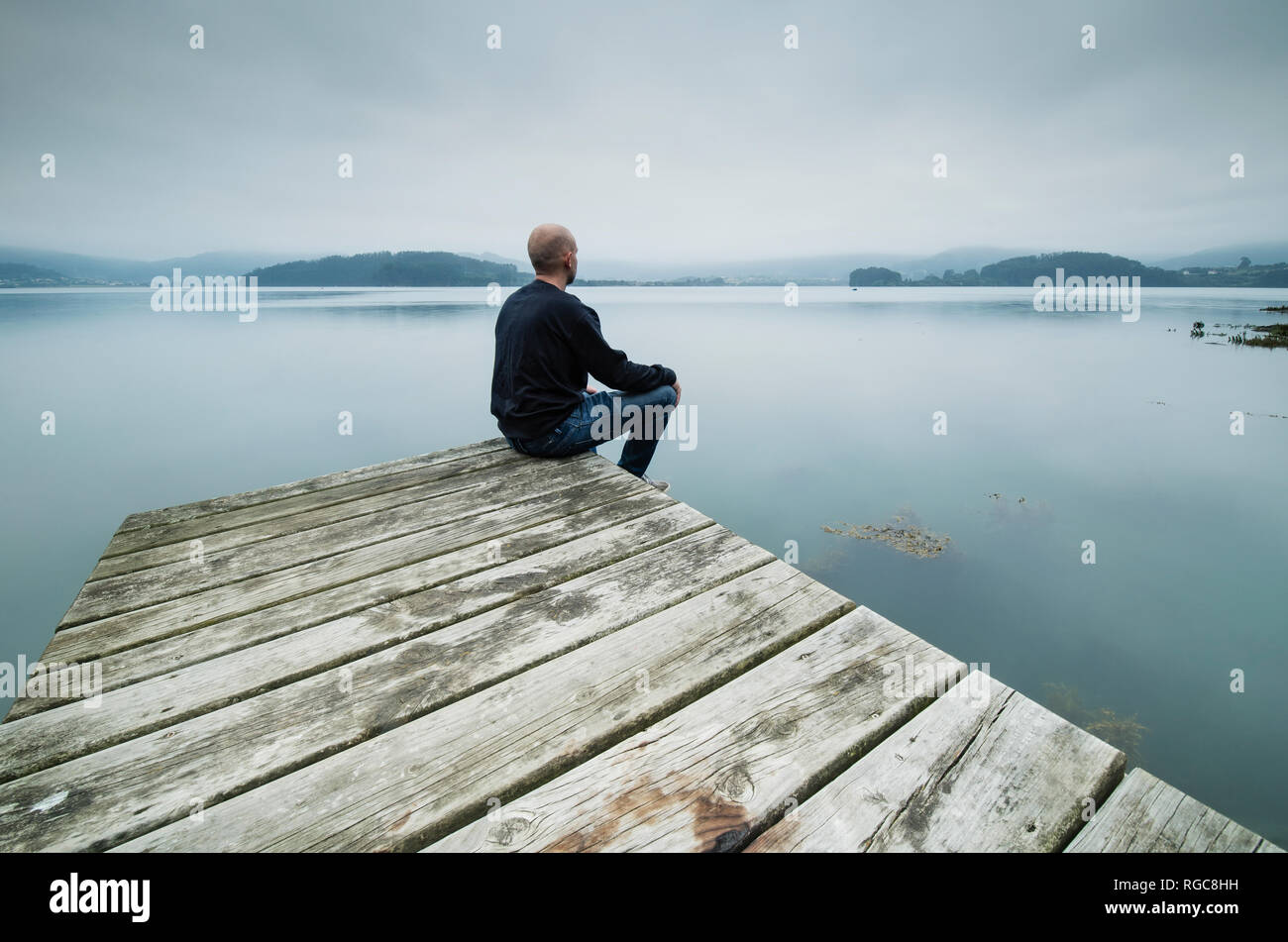Lonely man sitting on jetty looking at distance Stock Photo