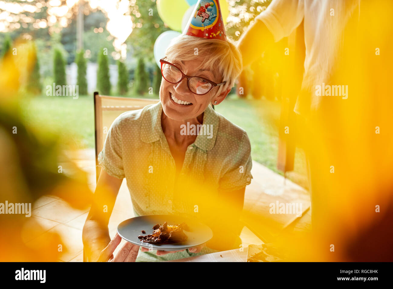 Smiling mature woman holding plate with cake on a birthday garden party Stock Photo