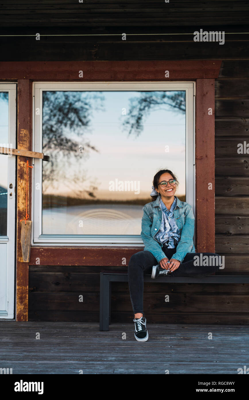Happy young woman sitting on veranda of a wooden house Stock Photo - Alamy