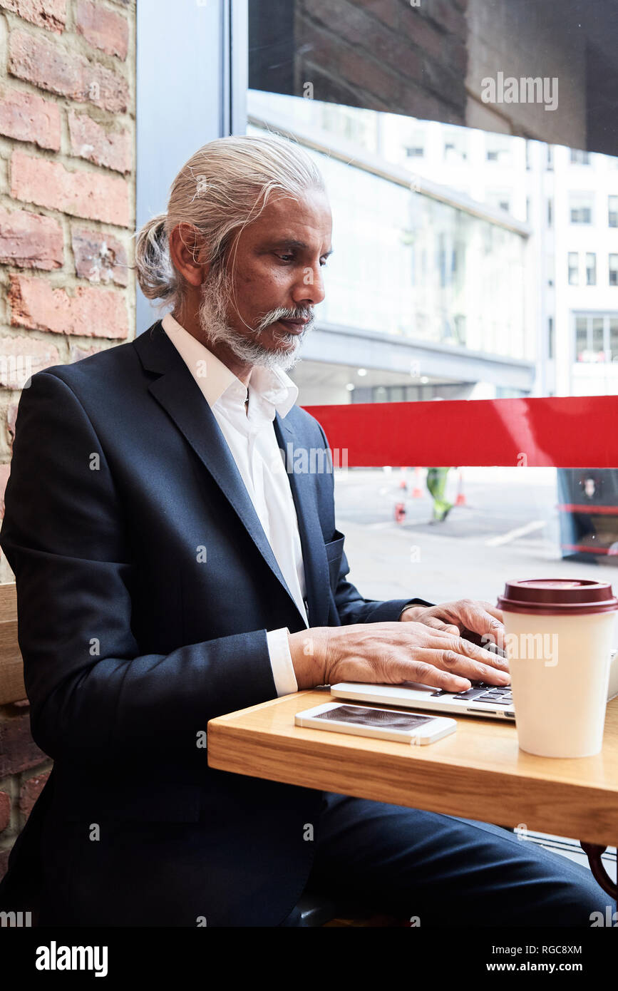 Senior businessman sitting in a coffee shop working on laptop Stock Photo