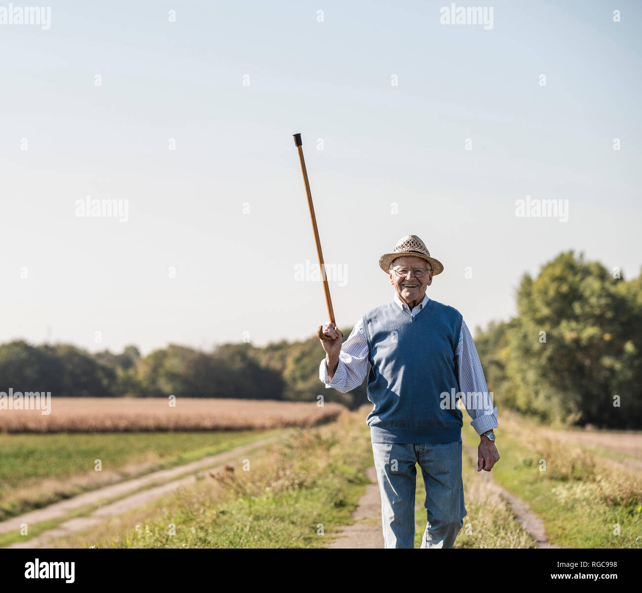 Senior man walking in the fields, greeting with his walking stick Stock Photo