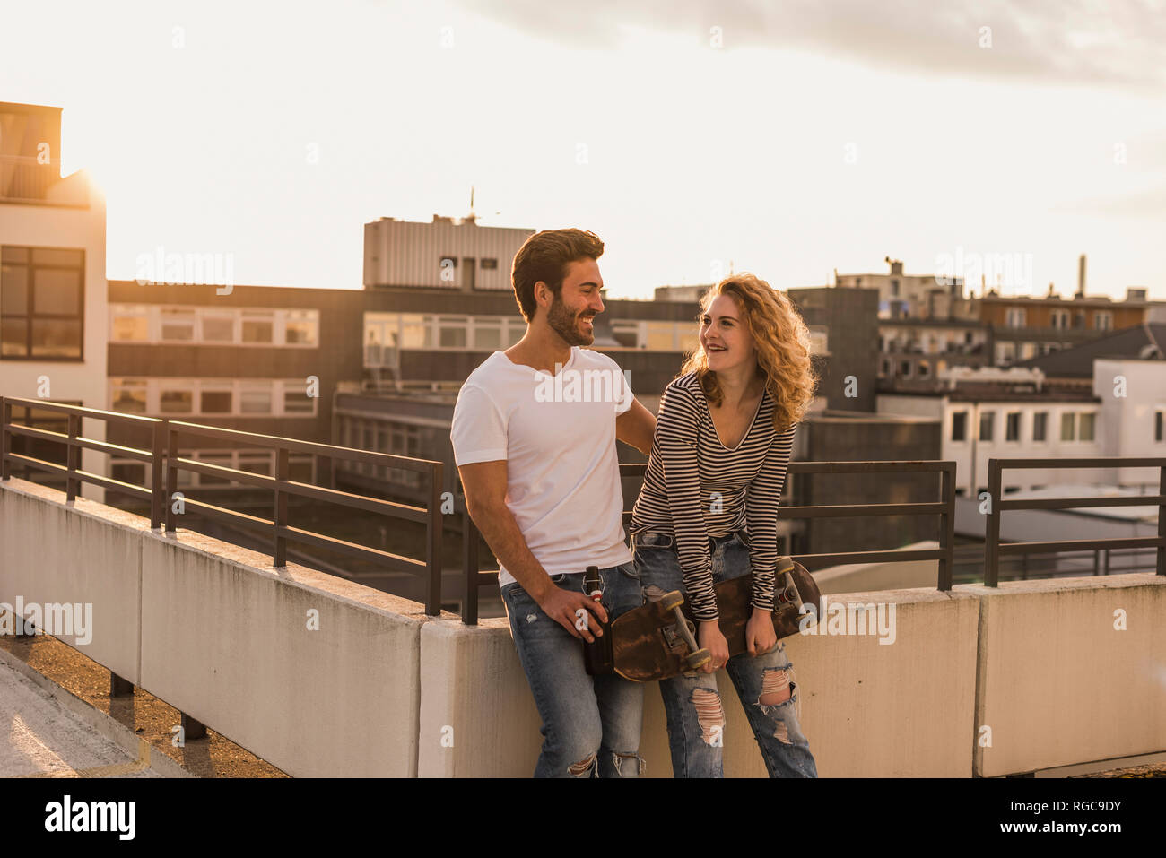Happy young couple relaxing on roof terrace at sunset Stock Photo