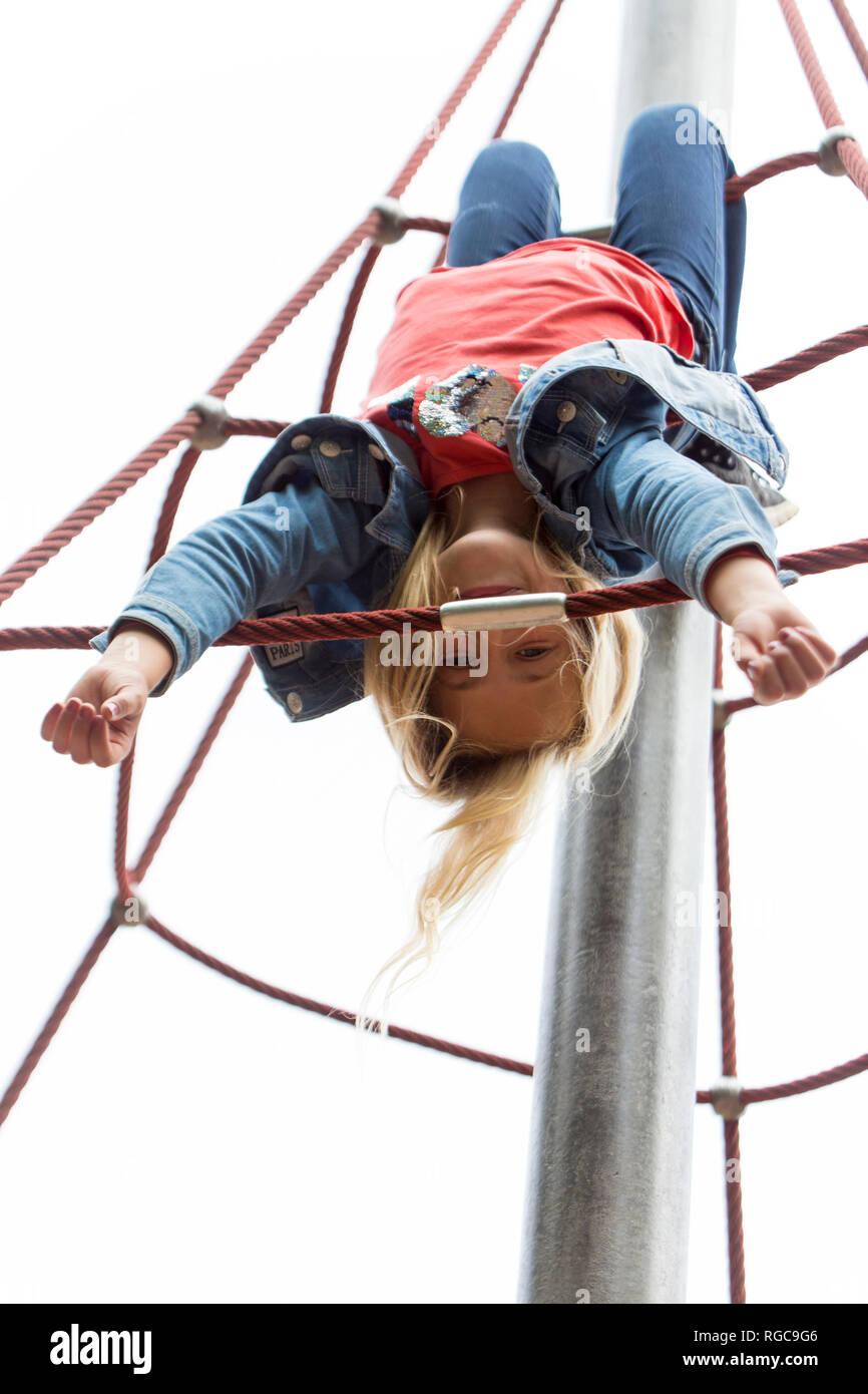Blond girl hanging upside down on jungle gym at playground Stock Photo