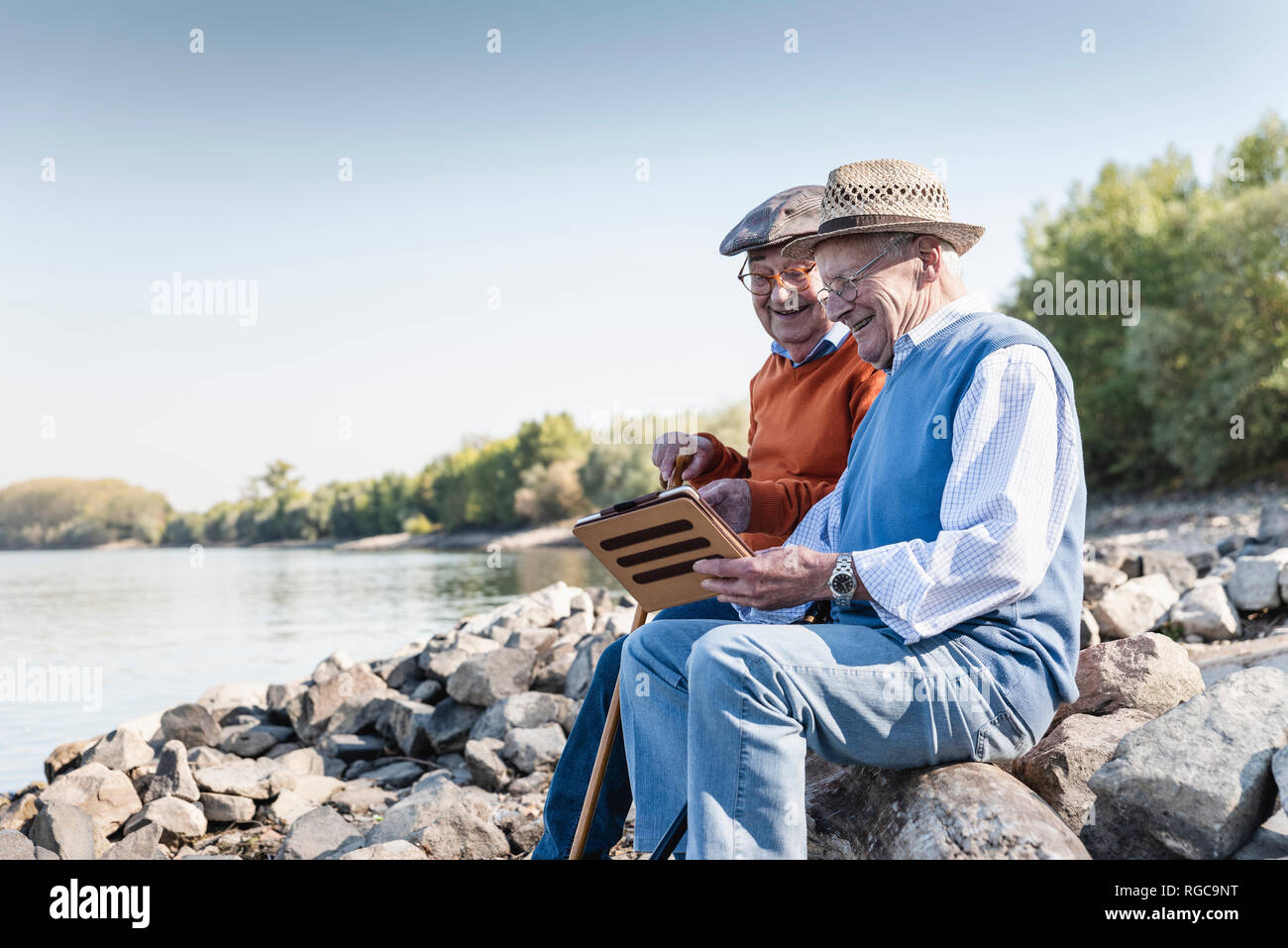 Two old friends sitting by the riverside, using digital tablet Stock Photo