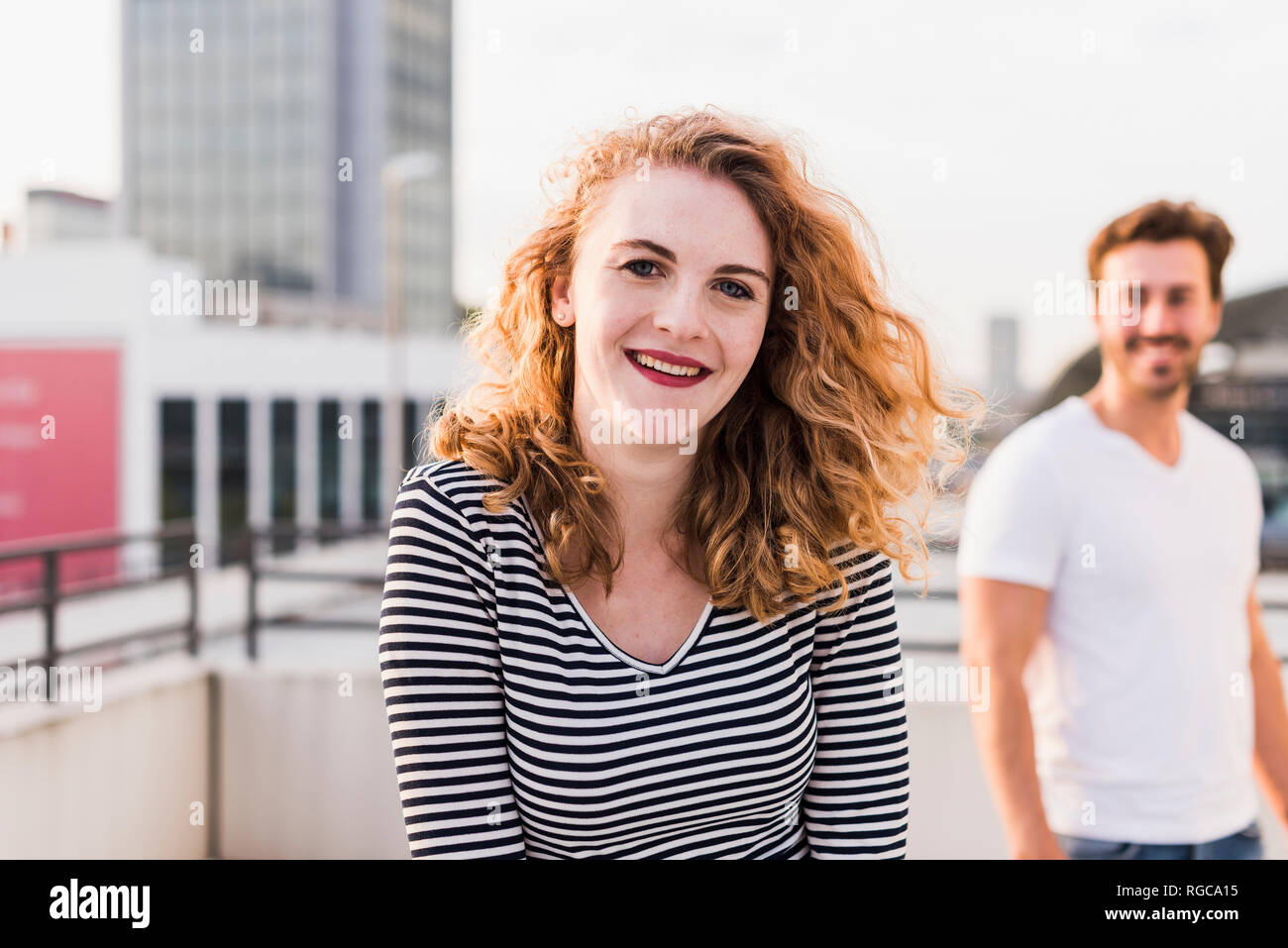 Portrait of happy young woman with boyfriend in the background at sunset Stock Photo