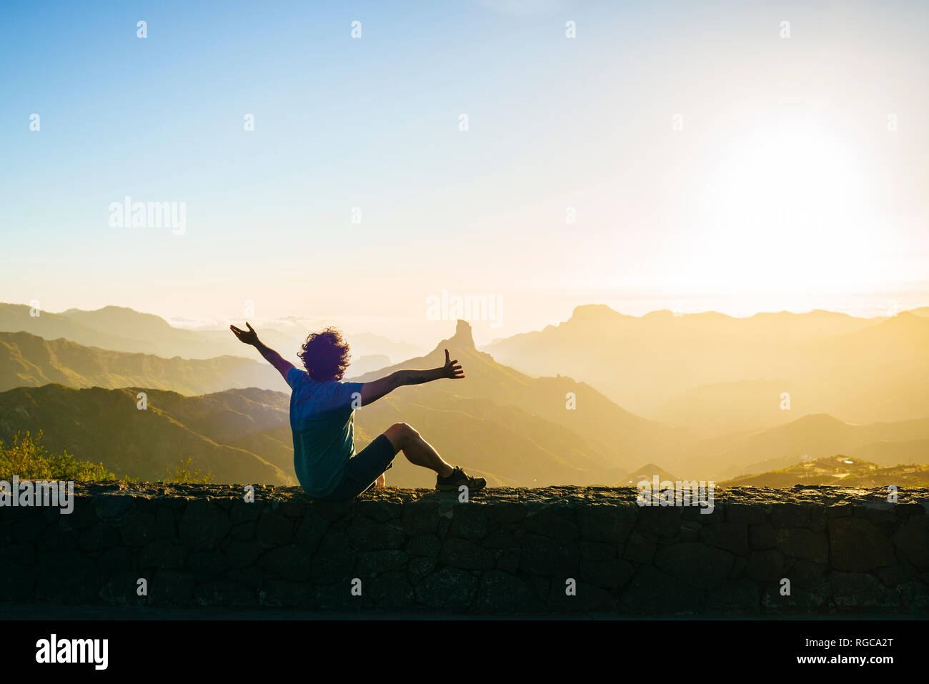 Spain, Canary Islands, Gran Canaria, back view of happy man watching mountain landscape at sunset Stock Photo