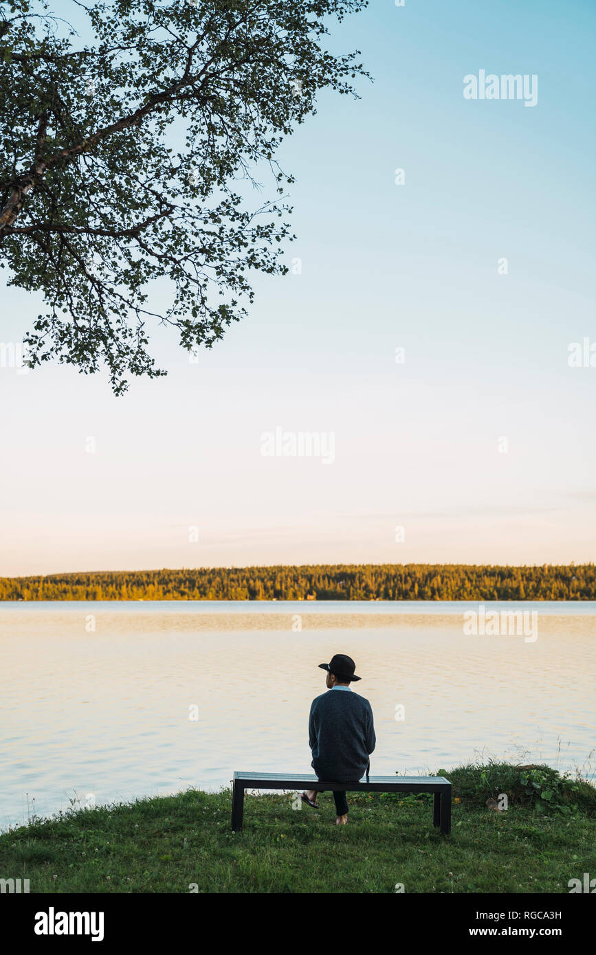 Young man sitting on a bench, looking at the lake Stock Photo
