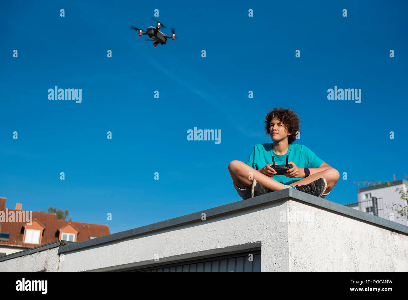 Boy navigating a flying drone, sitting on garage roof Stock Photo