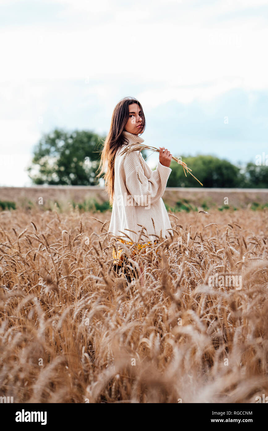 Young woman wearing oversized turtleneck pullover standing in corn field Stock Photo