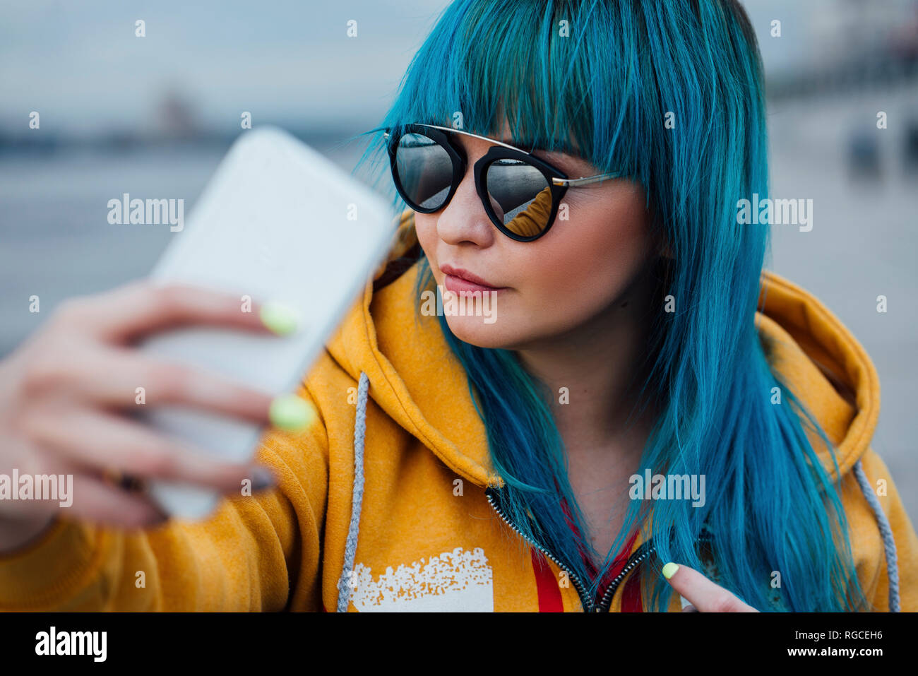 Portrait of young woman with dyed blue hair taking selfie with smartphone Stock Photo