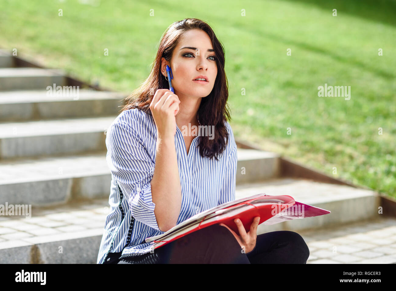 Portrait of pensive student with notebook sitting on stairs outdoors Stock Photo