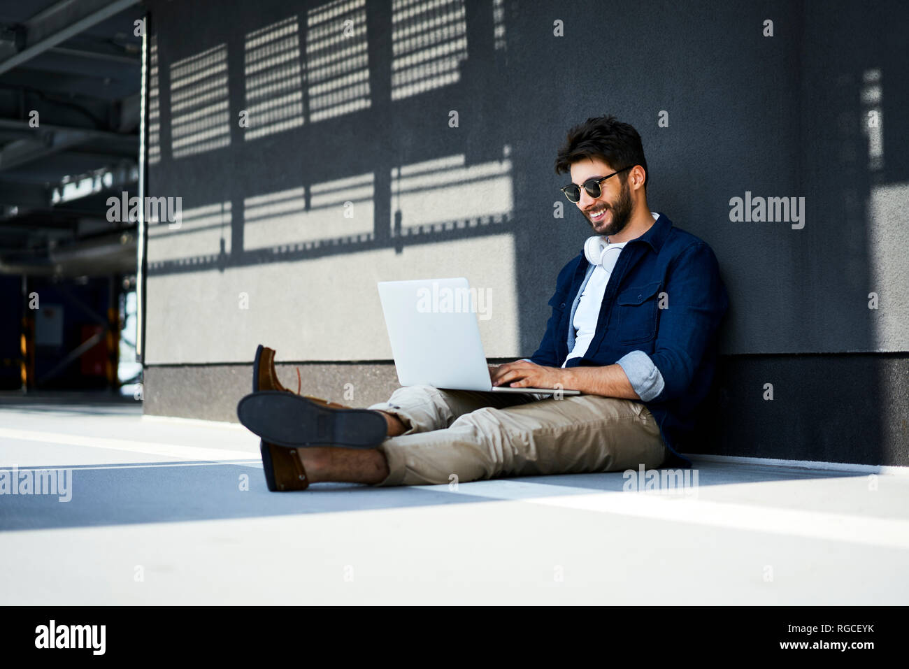 Relaxed young man sitting on the ground using laptop Stock Photo
