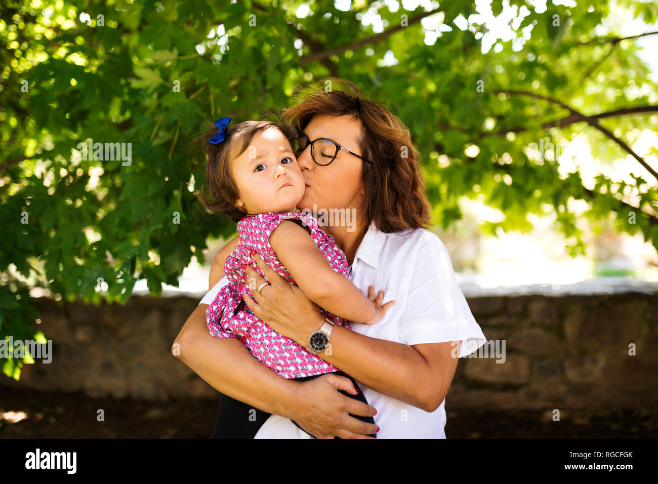 Mature woman kissing serious baby girl Stock Photo